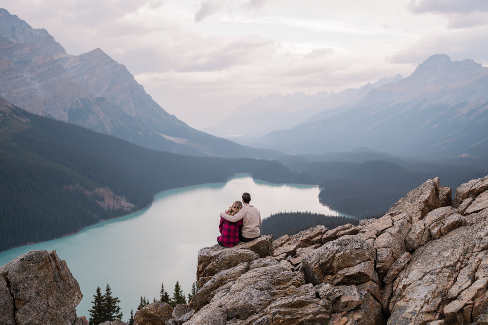 couple sits on rocks and cuddles and looks out over Peyto Lake in Banff National Park