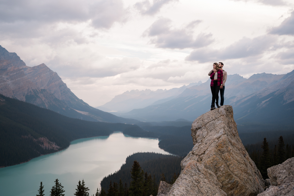 Couple cuddles on tall rock standing above Peyto Lake in Banff National Park