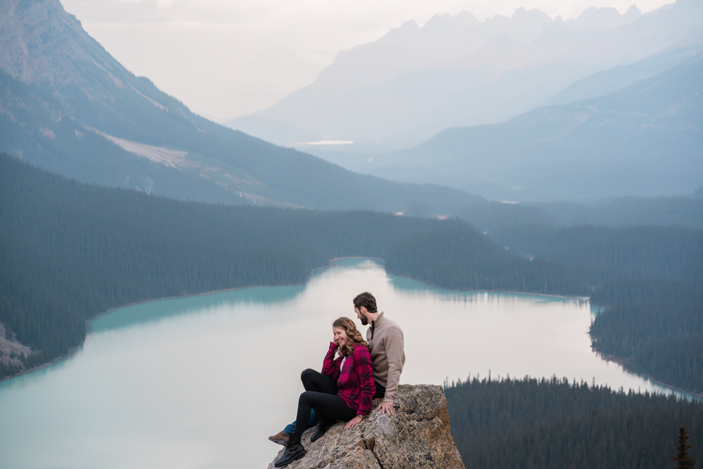 couple sits on rock during a Banff proposal session and laughs together