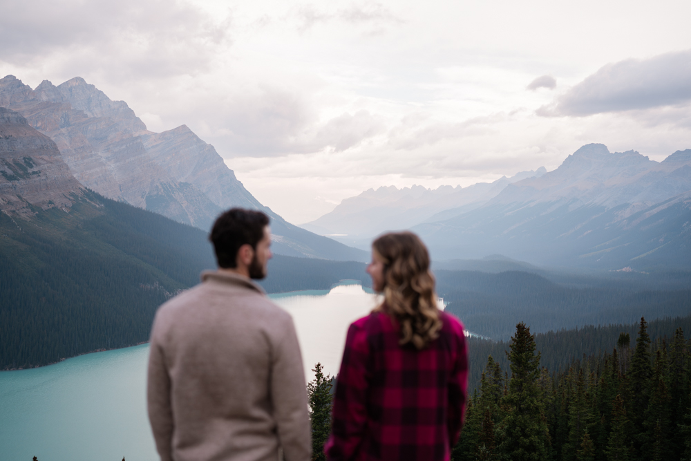 couple in foreground look at each other out of focus while the focus is on the lake and the mountains behind them in Banff National Park