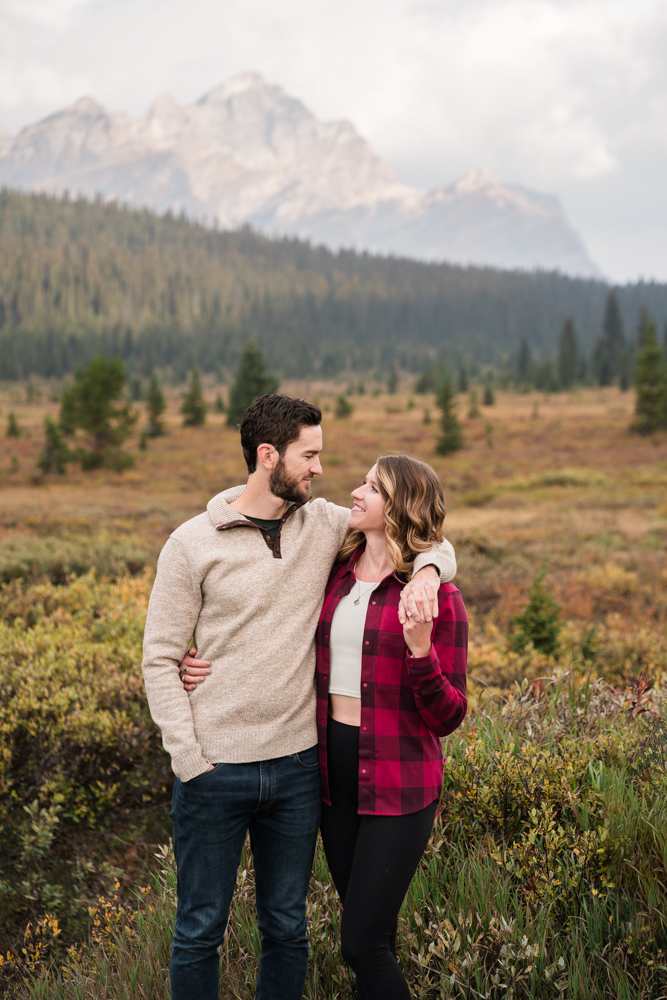 Couple stands in field in Banff National Park with all the fall colours around them