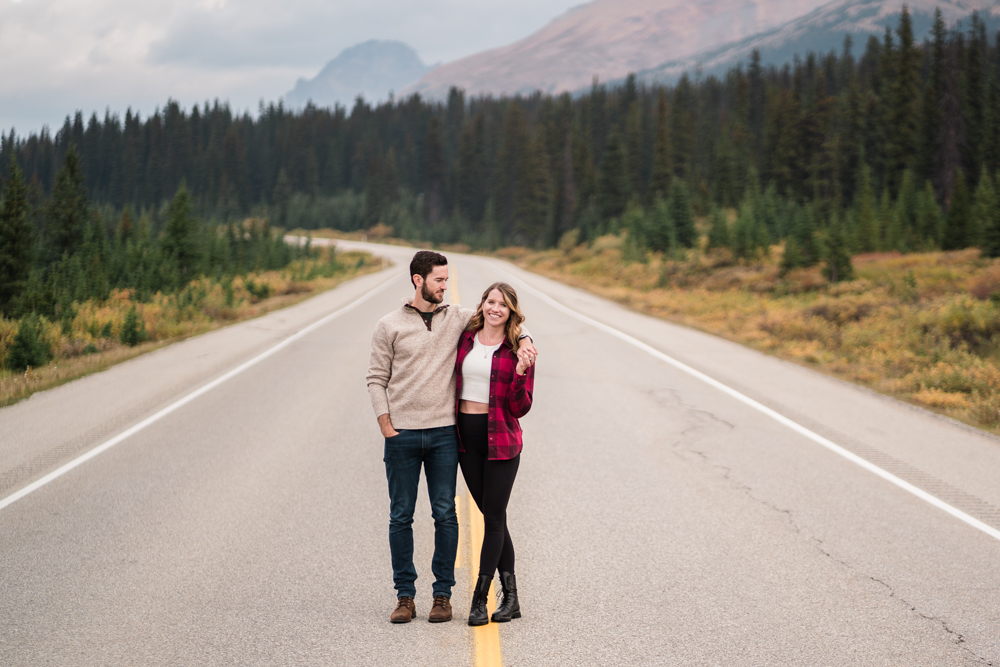 Couple stands on center line of road in Banff National Park cuddling during a Peyto Lake Engagement session