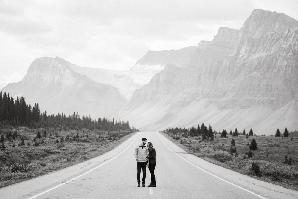 Black and white photo of couple standing over the center line on the Icefield's Parkway during a Banff Engagement Session