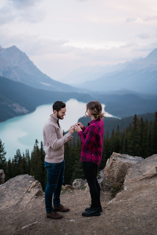 man slides ring on womans finger during a Peyto Lake engagement session.