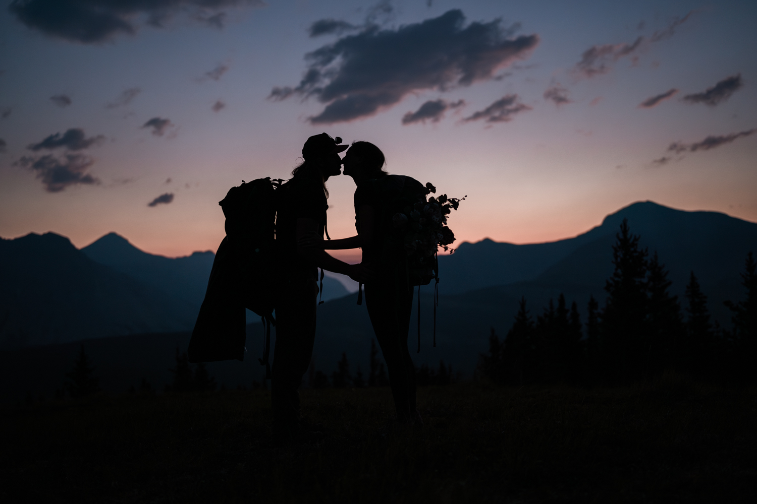 Couple kisses in the dark as the sky lightens behind them during sunrise hiking elopement in Kananaskis. 