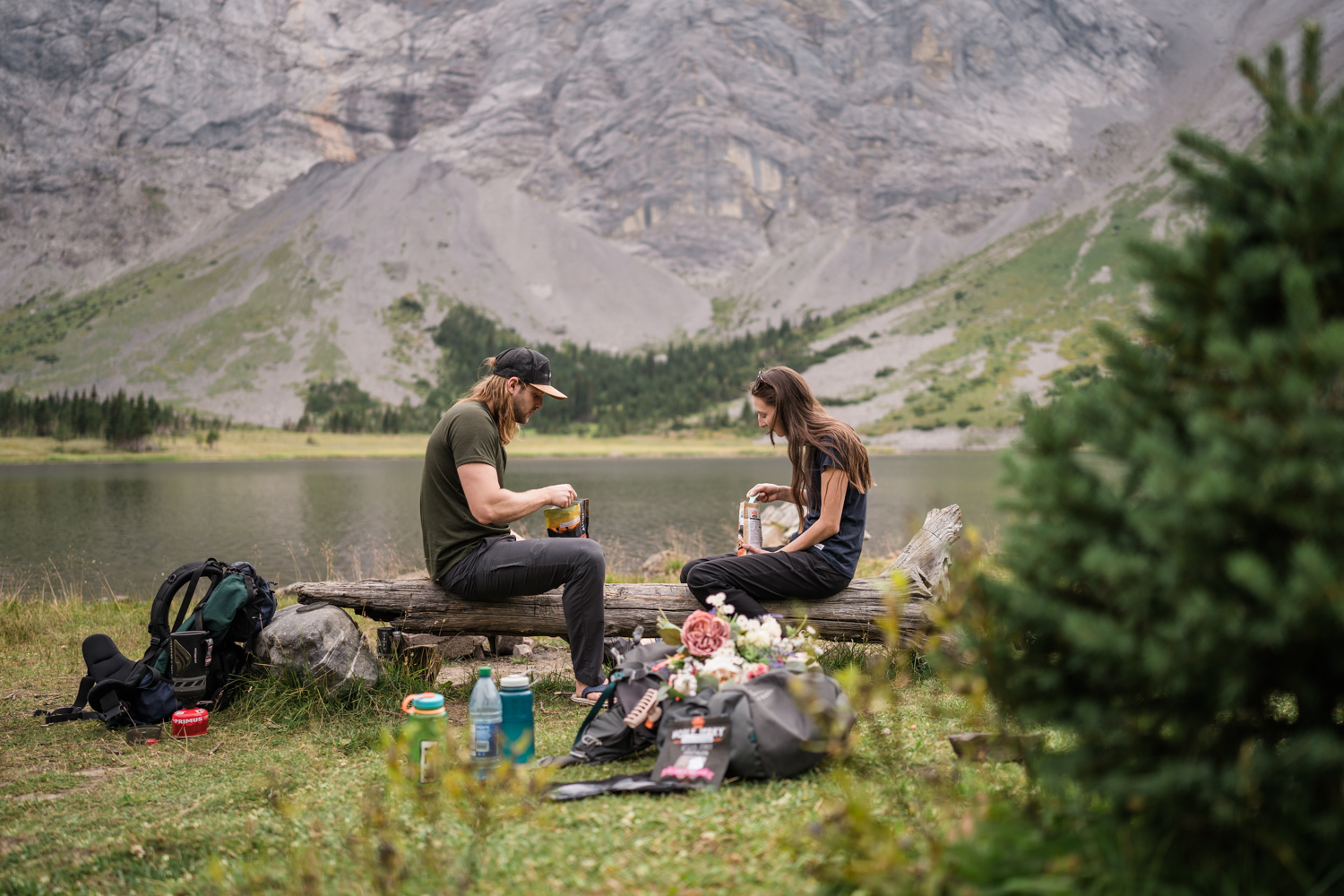 couple sits on a log eating dinner while backpacking for their elopement in Albetra
