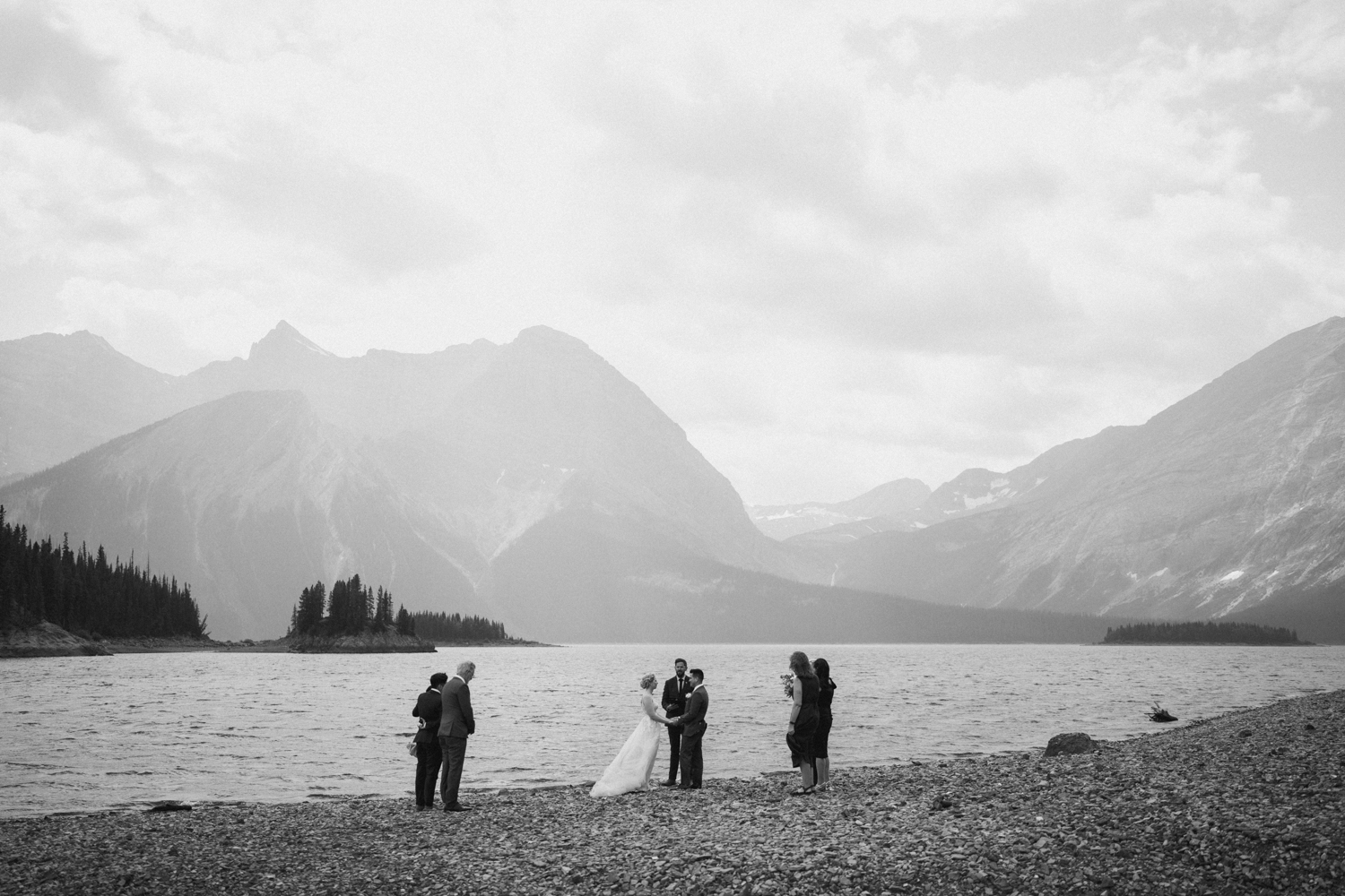 black and white photo of a wedding ceremony with 6 people in front of upper kananaskis lake
