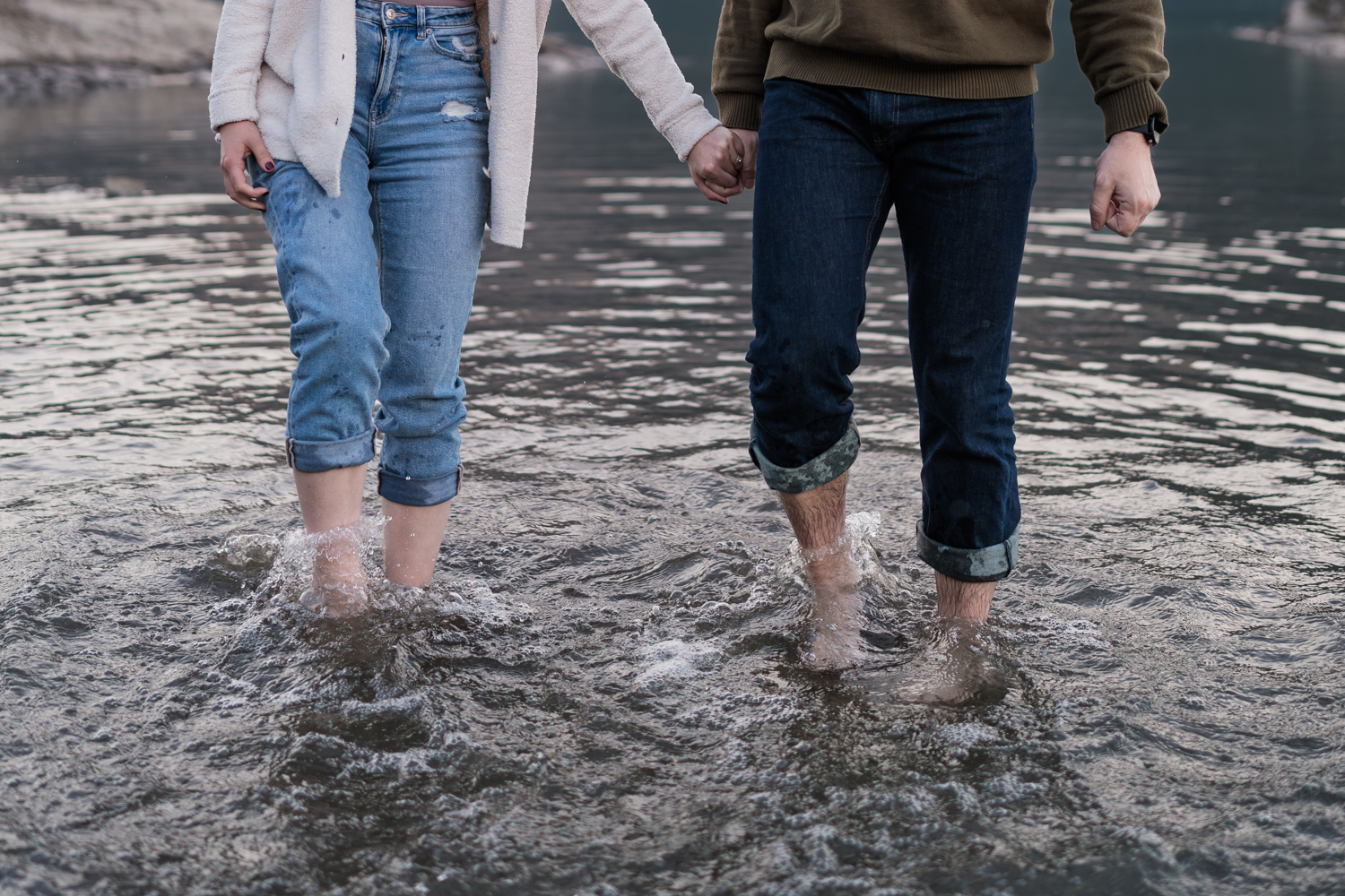 Couple holds hands and kicks their feet in the water. 