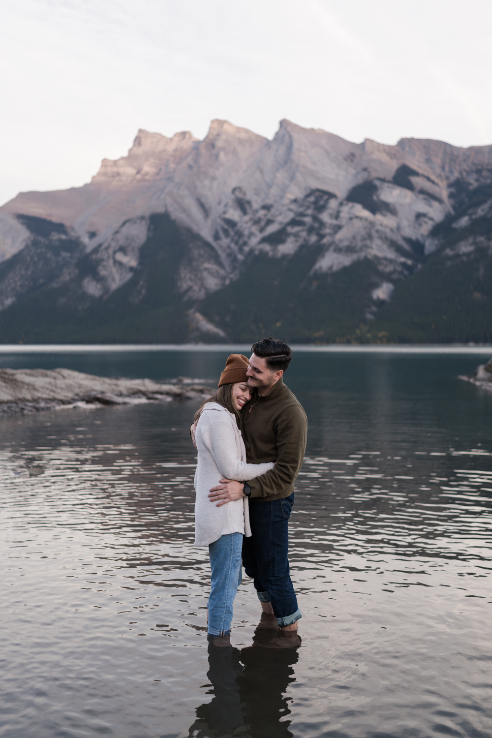 Couple stands in Lake Minnewanka together after sunset Banff Proposal.